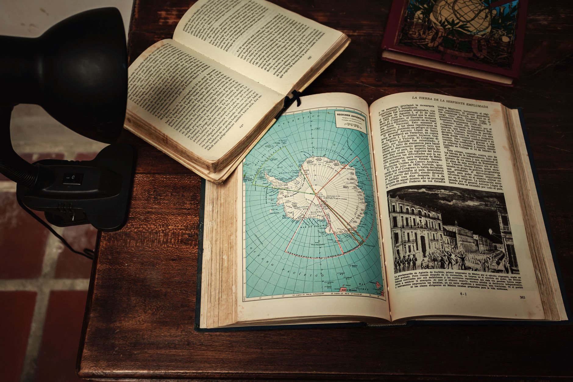 Open book on a vintage wooden desk under warm, amber library light